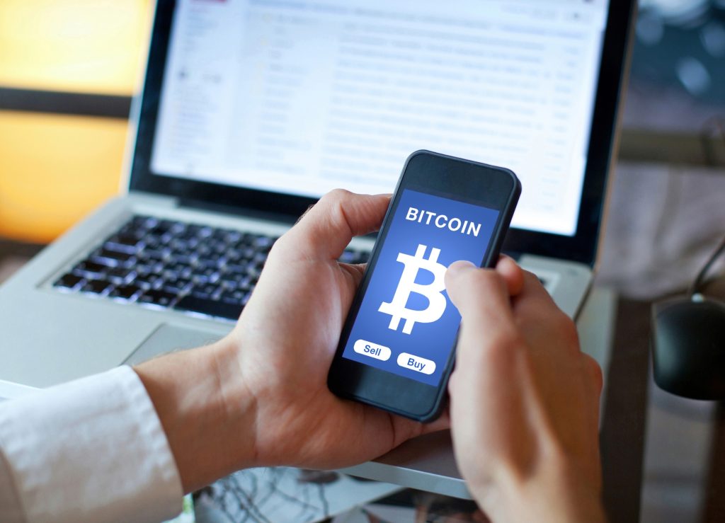 Image of a hand holding a mobile phone showing a symbol of the bitcoin cryptocurrency.
